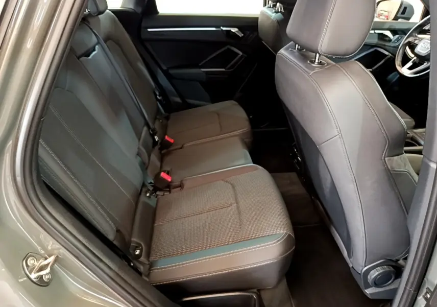 Vue intérieure côté arrière gauche de l’Audi Q3 gris foncé, montrant la banquette arrière en tissu et cuir avec ceintures rouges.