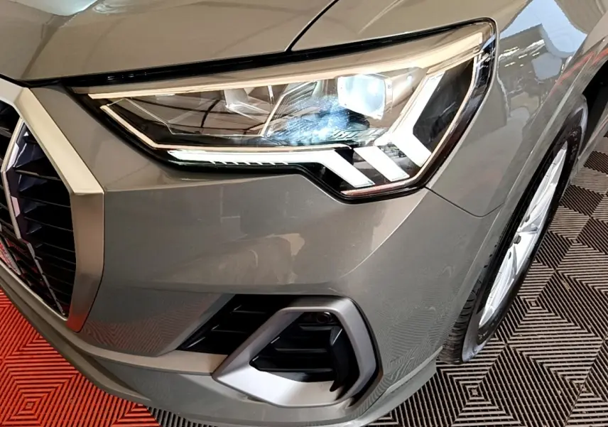 Gros plan sur le phare avant droit d’un Audi Q3 gris foncé 35 TFSI S Line avec calandre et antibrouillard visibles.