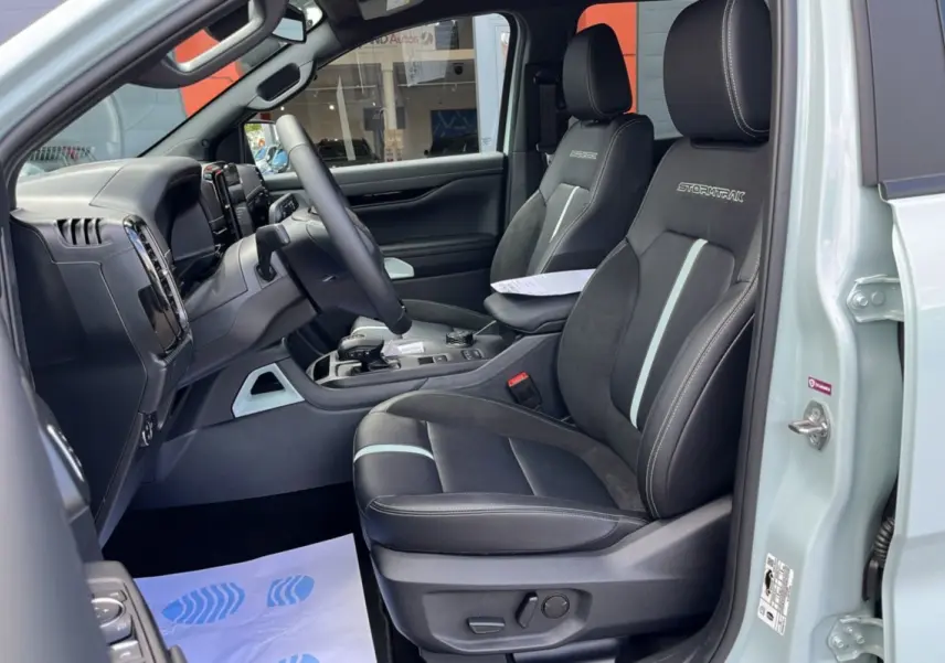 Vue intérieure côté conducteur du Ford Ranger gris zen 2026, sièges Stormtrak noirs avec surpiqûres blanches et volant multifonctions.