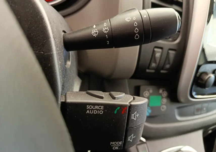 Gros plan sur la commande audio au volant du Renault Trafic Fourgon blanc, avec levier d’essuie-glace en arrière-plan.