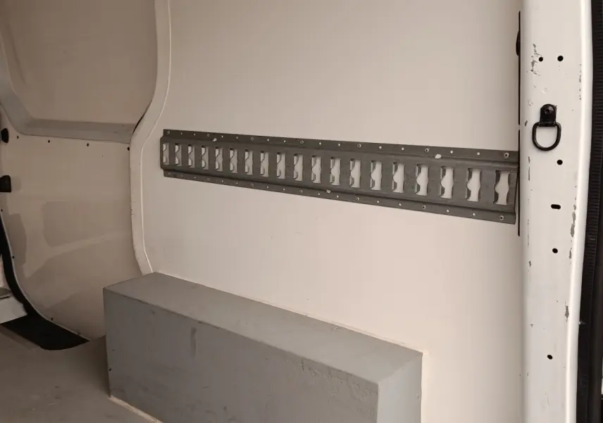 Vue intérieure côté droit du fourgon blanc Renault Trafic, montrant la cloison pleine et un rail métallique mural.