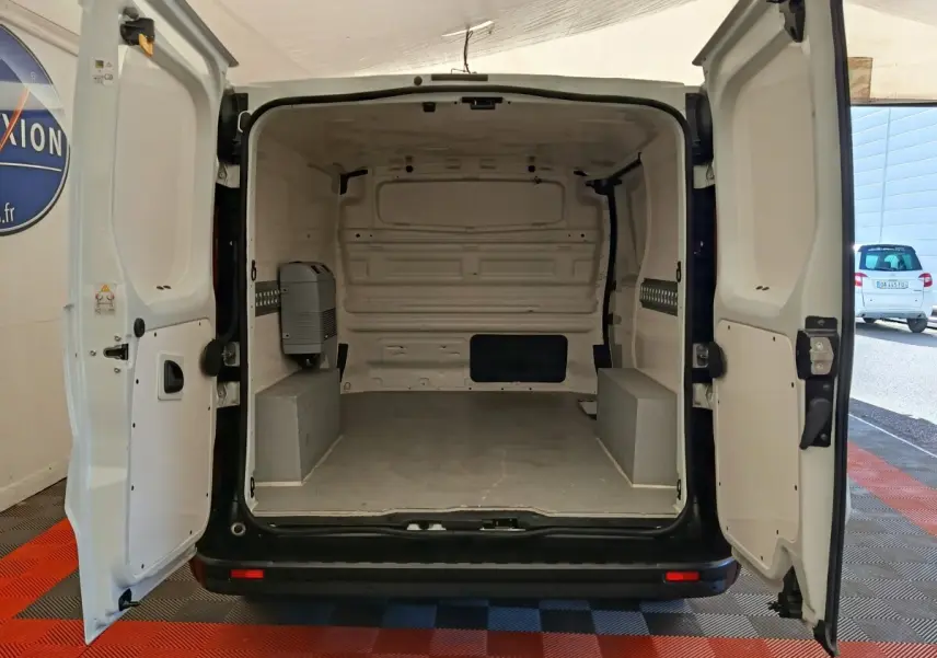 Vue arrière du fourgon Renault Trafic blanc 2017 avec portes ouvertes montrant l'espace de chargement vide et cloison pleine.