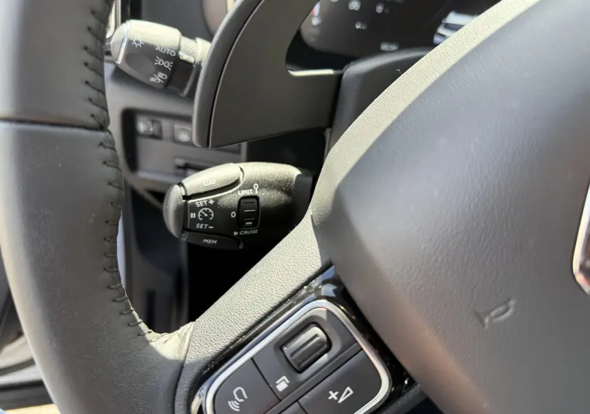 Gros plan sur la commande de régulateur de vitesse à gauche du volant gris du Citroën C5 Aircross Hybrid 2025.