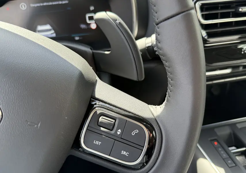 Gros plan sur le volant en cuir noir du Citroën C5 Aircross Hybrid 2025, avec commandes intégrées et palettes de changement de vitesse.