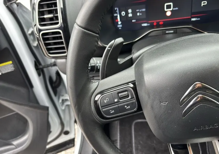 Vue rapprochée du volant noir du Citroën C5 Aircross Hybrid 2025, avec commandes intégrées et tableau de bord numérique visible.