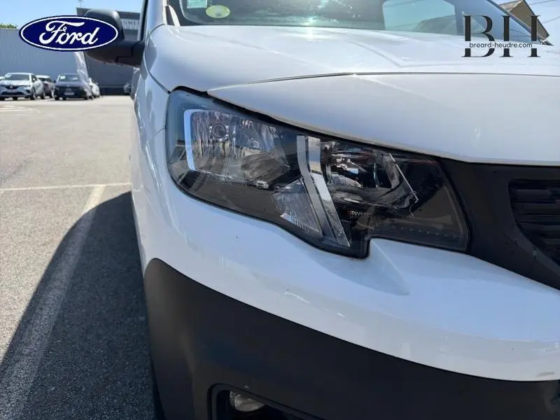 Gros plan sur le phare avant droit du Peugeot Partner blanc, mettant en valeur le design moderne et le pare-chocs noir.
