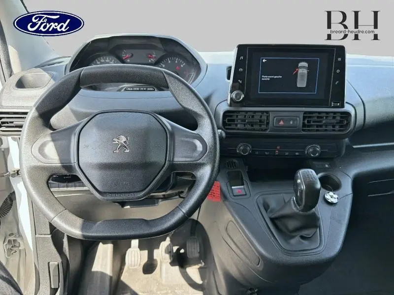 Vue intérieure du poste de conduite du Peugeot Partner blanc 2019, avec volant, écran tactile et levier de vitesse manuel visibles.