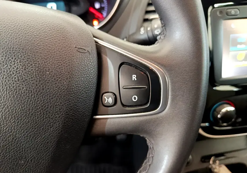 Gros plan sur les commandes du volant cuir du Renault Captur Business gris foncé, avec écran tactile et tableau de bord en arrière-plan.