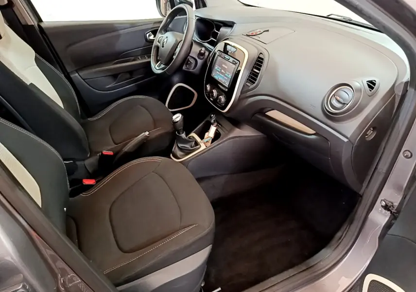 Vue intérieure côté conducteur du Renault Captur gris foncé, montrant tableau de bord avec écran tactile et volant cuir multifonctions.