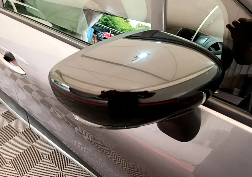 Gros plan sur le rétroviseur côté gauche noir brillant du Renault Captur gris foncé, avec reflet de l'environnement intérieur.