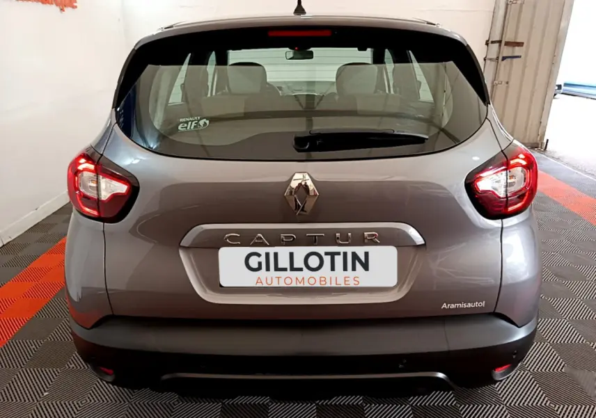 Vue arrière d'un Renault Captur gris foncé avec feux arrière allumés et logo centré sur le hayon.