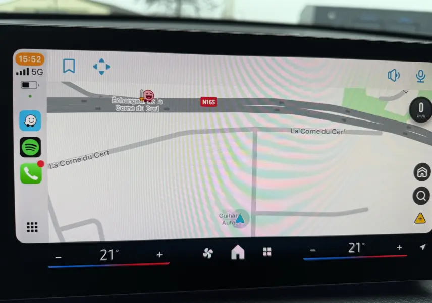 Écran de navigation intérieur d'un BMW X1 blanc minéral, affichant une carte routière avec commandes climatisation à 21°C.
