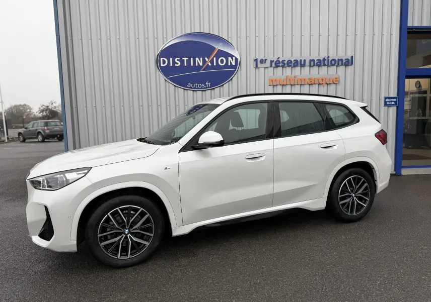 BMW X1 18D M Sport blanc minéral vu de profil côté gauche, avec jantes alliage et logo M Sport visible.