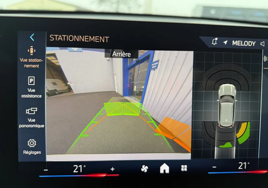 Vue caméra de recul avec guidage vert et orange sur un BMW X1 blanc Mineral en stationnement arrière.