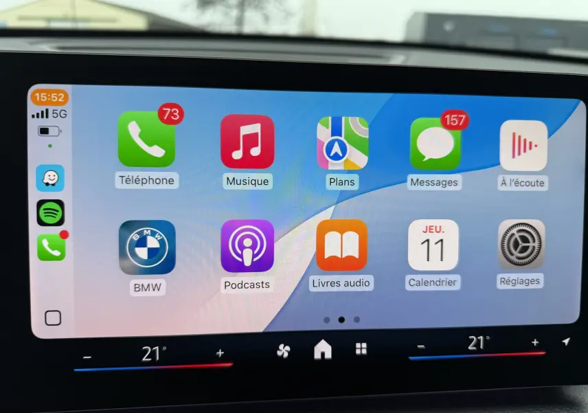 Écran tactile central affichant les applications connectées dans un BMW X1 blanc Mineral, vue intérieure frontale.