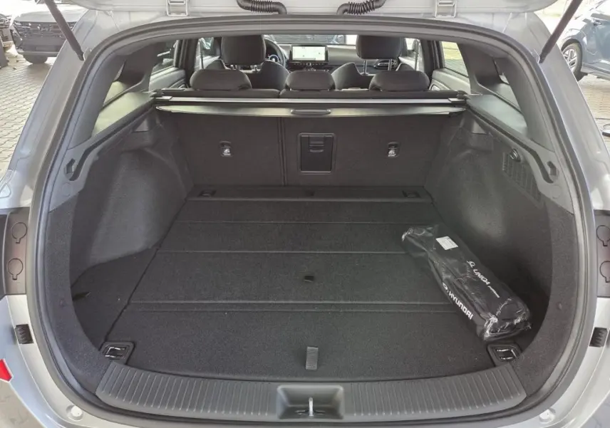 Vue arrière du coffre ouvert d'une Hyundai i30 SW N-LINE gris foncé, montrant un espace de chargement spacieux et un kit Hyundai.
