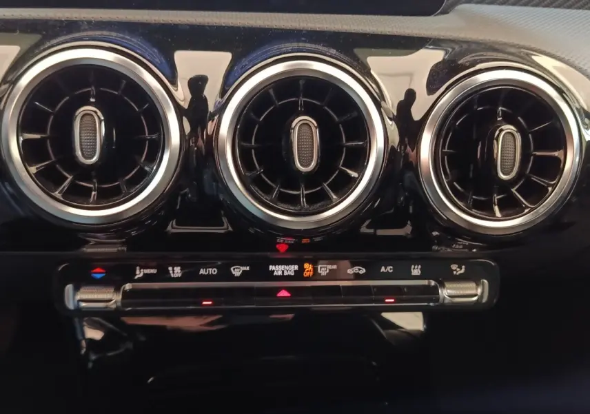Gros plan sur les trois aérateurs ronds chromés et la commande de climatisation du tableau de bord noir brillant du Mercedes GLA 250 e.