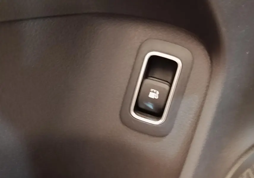 Gros plan sur le bouton d'ouverture de trappe à carburant dans l'habitacle du Mercedes GLA 250 e gris foncé.