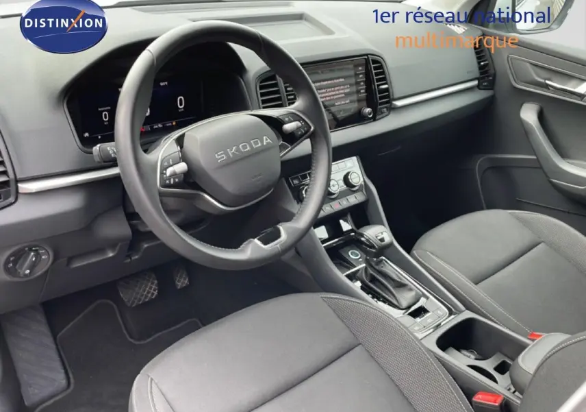 Vue intérieure côté conducteur du Skoda Karoq blanc glacier 2025, avec volant multifonction et console centrale moderne.