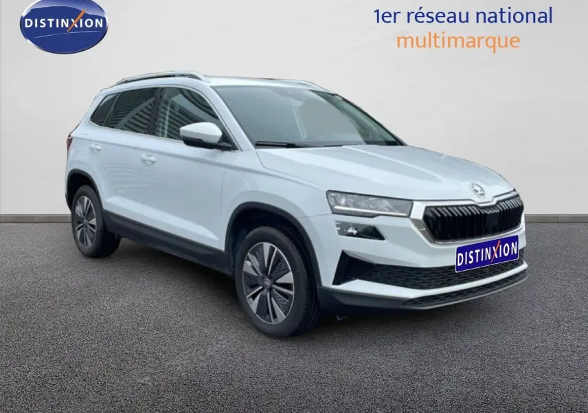 Vue 3/4 avant droite d’un Skoda Karoq blanc glacier 2025 avec calandre noire et jantes bi-ton.