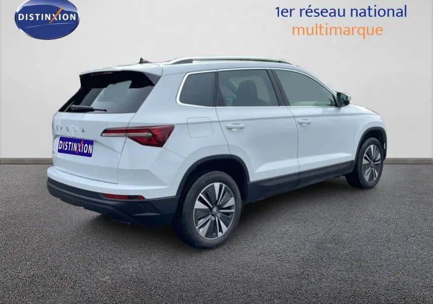 Vue 3/4 arrière droite d'un Skoda Karoq blanc glacier 2025 avec jantes bi-ton et toit noir contrasté.