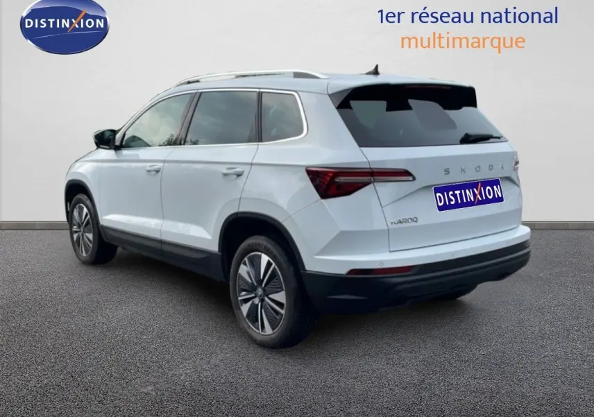 Vue 3/4 arrière droite d’un Skoda Karoq blanc glacier avec jantes alliage et vitres teintées sur fond neutre.