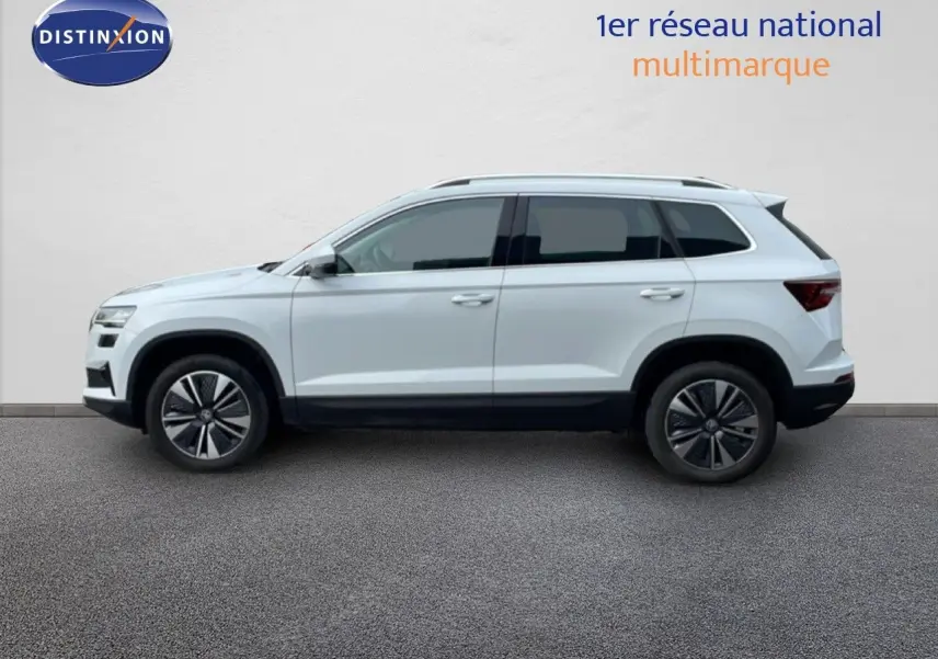 Profil droit d’un Skoda Karoq blanc glacier 2025 avec jantes alliage bicolores sur fond neutre.