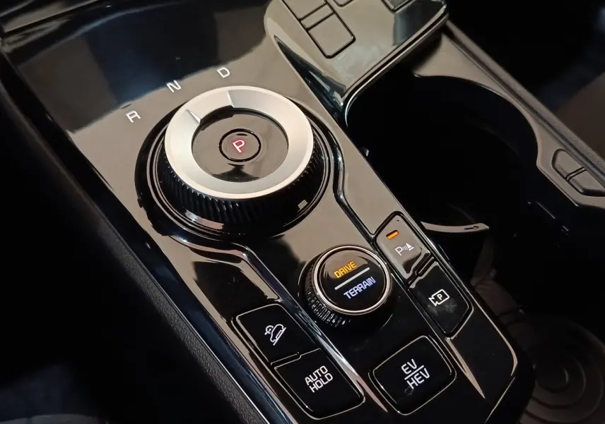 Gros plan sur la console centrale noire du KIA SPORTAGE hybride rechargeable avec sélecteur de mode de conduite et bouton de frein à main.