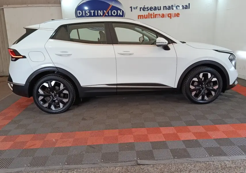 Vue profil côté gauche d’un Kia Sportage blanc 2022 hybride rechargeable avec jantes noires et toit blanc.