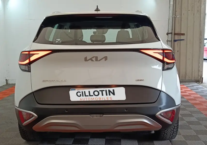 Vue arrière d’un Kia Sportage blanc hybride rechargeable avec feux LED allumés dans un garage.