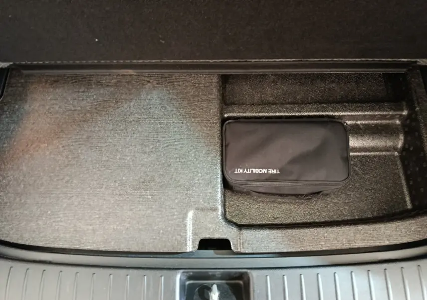 Coffre ouvert du Kia Sportage blanc, vue plongeante sur compartiment avec trousse de mobilité noire.