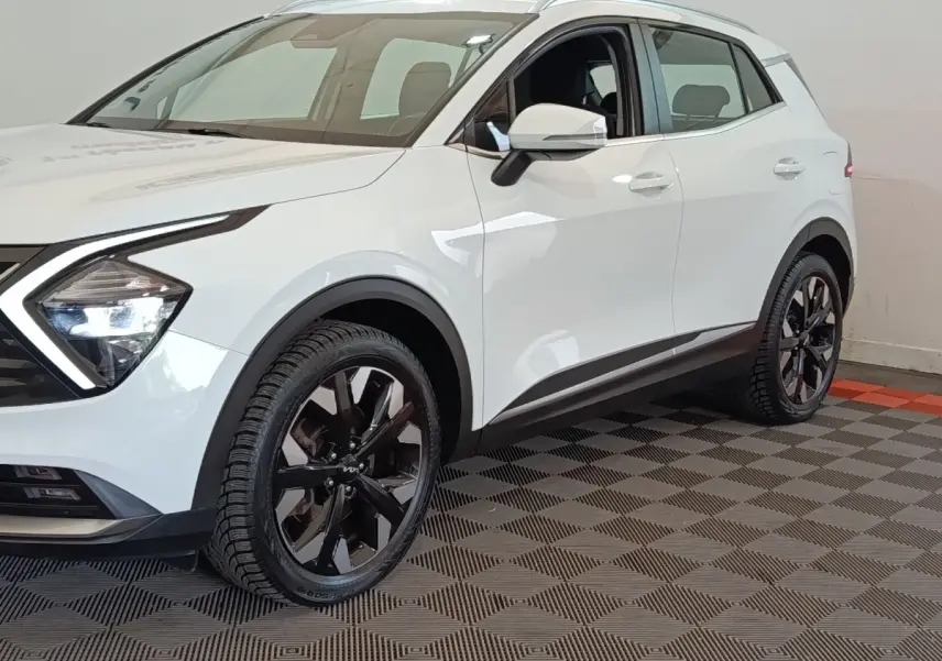 Vue 3/4 avant droit d'un KIA SPORTAGE blanc avec jantes noires et feux LED distinctifs.