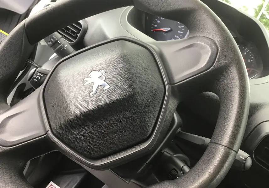 Gros plan sur le volant noir du Peugeot Partner 2022, avec logo lion argenté et tableau de bord en arrière-plan.