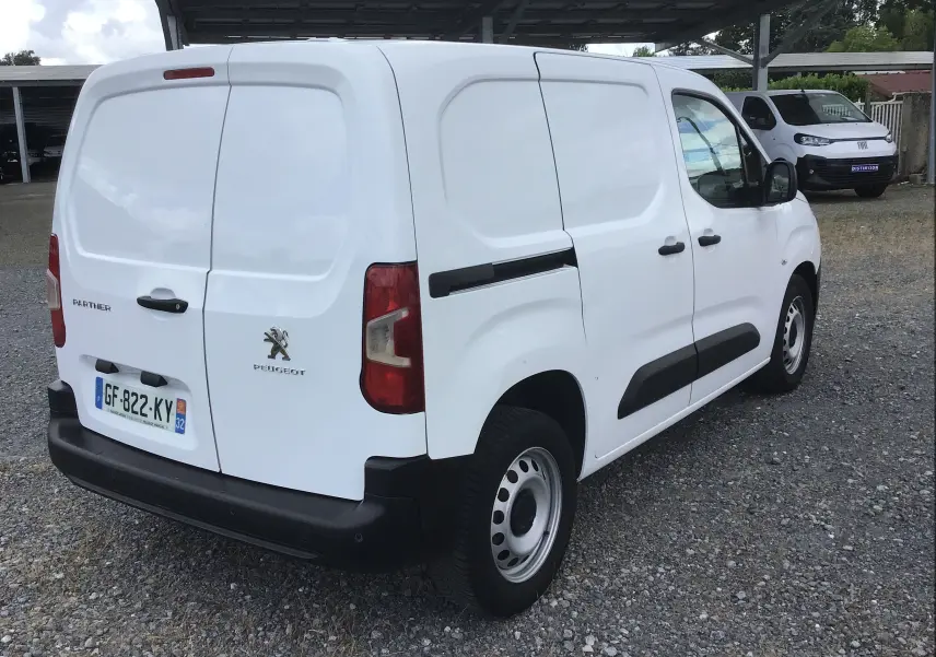 Vue 3/4 arrière droite d’un Peugeot Partner blanc utilitaire avec portes arrière battantes et protections noires.