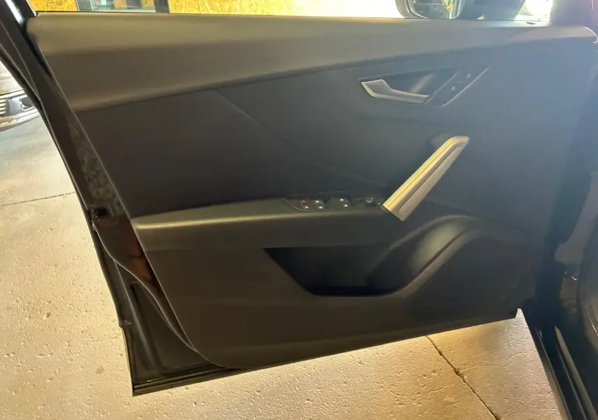 Vue intérieure du panneau de porte avant gauche noir de l'Audi Q2 2020, avec commandes électriques et poignée argentée.