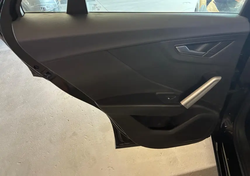 Vue intérieure de la porte arrière droite noire d'un Audi Q2 2020, avec poignée argentée et commande de fenêtre.