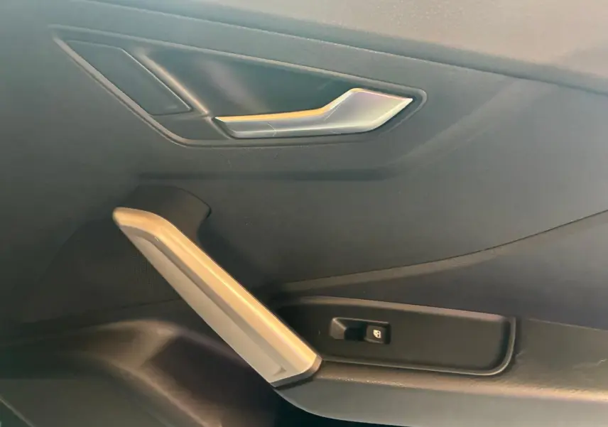 Gros plan sur la poignée intérieure côté gauche de la porte noire d’un Audi Q2 2020, avec bouton de commande de vitre.