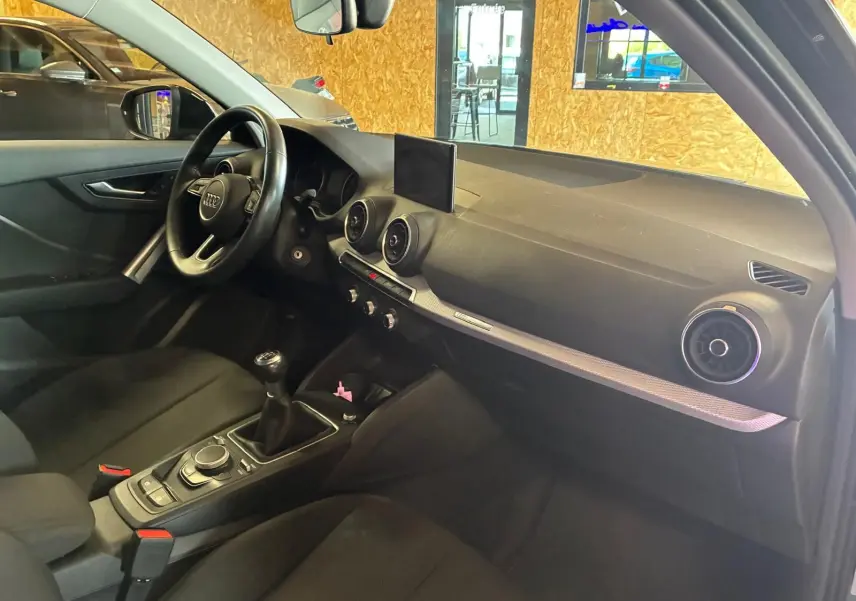 Intérieur noir de l’Audi Q2 30 1.6 TDI 2020 vu côté conducteur, avec tableau de bord et levier de vitesses manuel.
