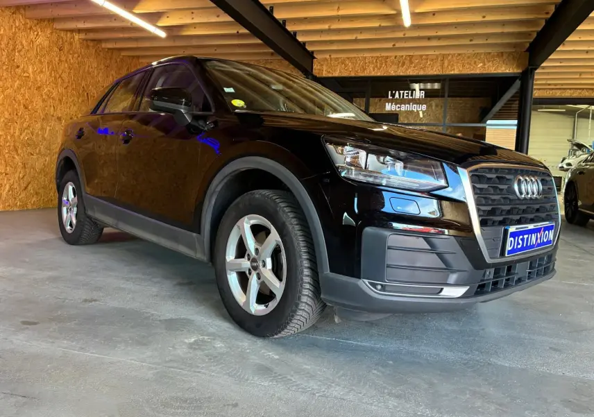Audi Q2 noir vue 3/4 avant droit dans un garage, mettant en valeur sa calandre distinctive et ses jantes argentées.