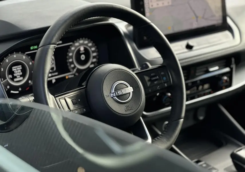 Vue rapprochée du volant cuir noir et du combiné numérique du Nissan Qashqai 2025, avec écran tactile de navigation.