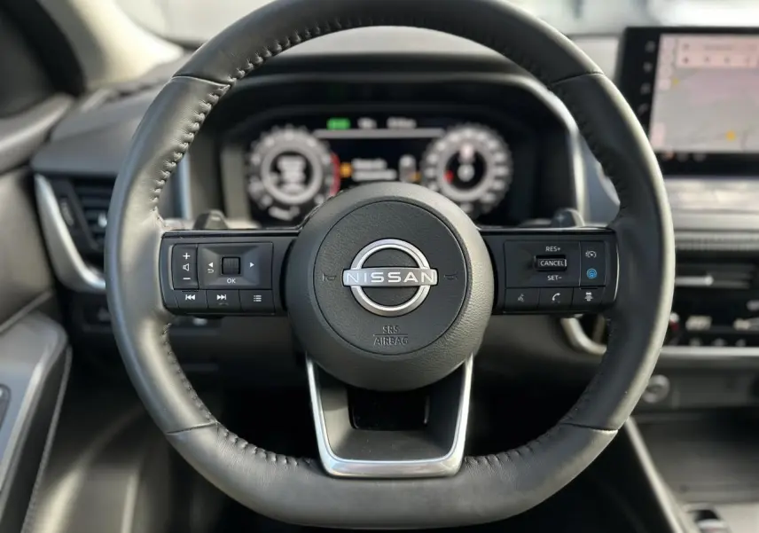 Vue rapprochée du volant cuir noir du Nissan Qashqai 2025 avec commandes intégrées et tableau de bord numérique flou.