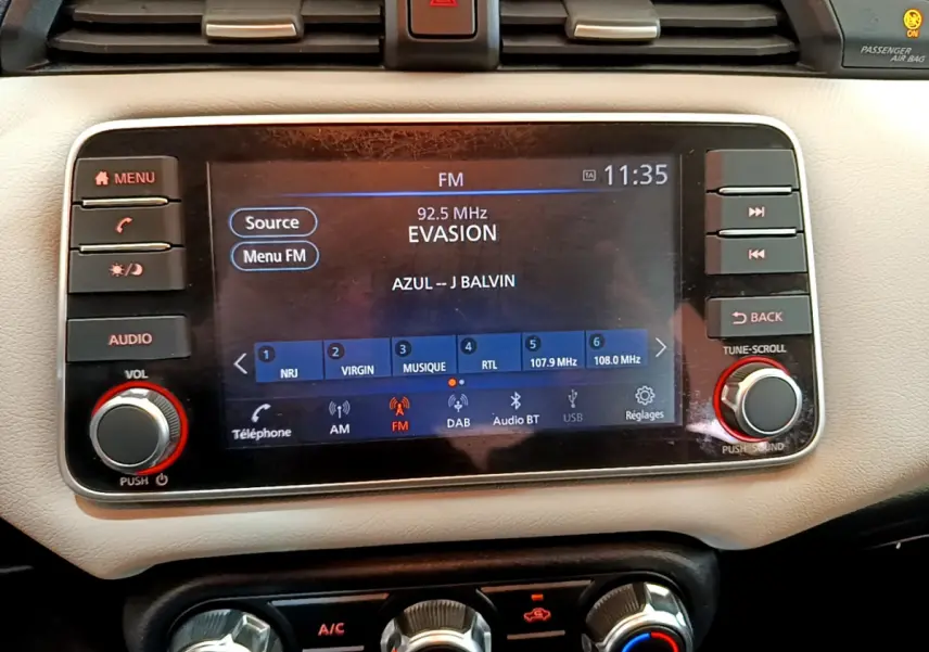 Écran tactile central allumé de la Nissan Micra blanche 2022, affichant la radio FM et commandes audio.