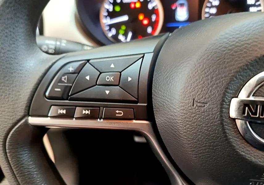 Gros plan sur le volant noir de la Nissan Micra IG-T 92 Acenta 2022 avec commandes multifonctions et tableau de bord lumineux.