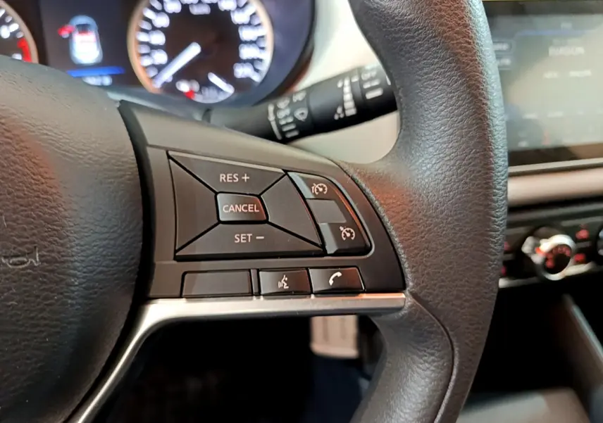 Gros plan sur le volant noir de la Nissan Micra IG-T 92 Acenta 2022, avec commandes de régulateur de vitesse et téléphone.