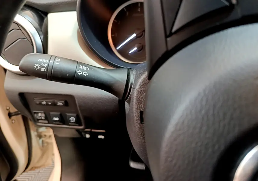 Gros plan sur la manette de clignotants et le tableau de bord noir du Nissan Micra blanc, côté gauche du volant.