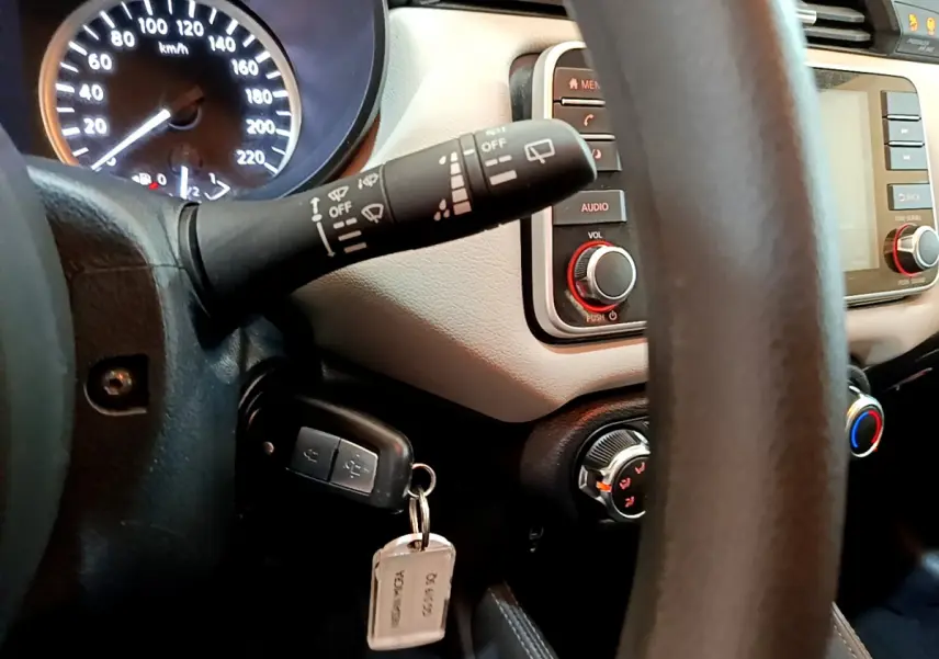 Vue rapprochée du tableau de bord et du volant d'une Nissan Micra blanche, avec clé insérée et commandes visibles.