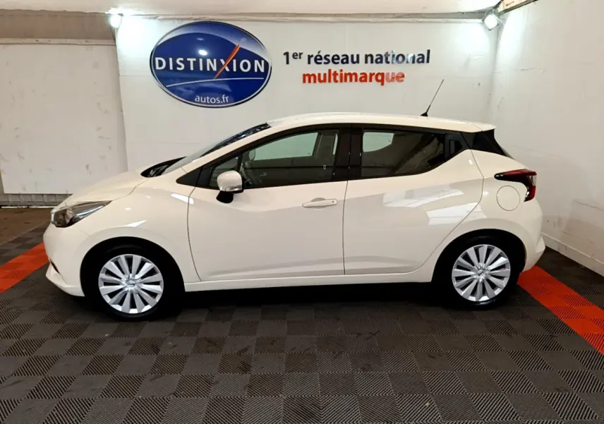 Profil côté gauche d'une Nissan Micra IG-T 92 Acenta blanche 2022, en intérieur sur sol damier noir et orange.