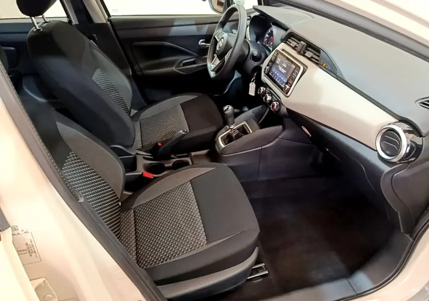 Vue intérieure côté conducteur de la Nissan Micra blanche 2022, montrant tableau de bord et sièges noirs à motifs.