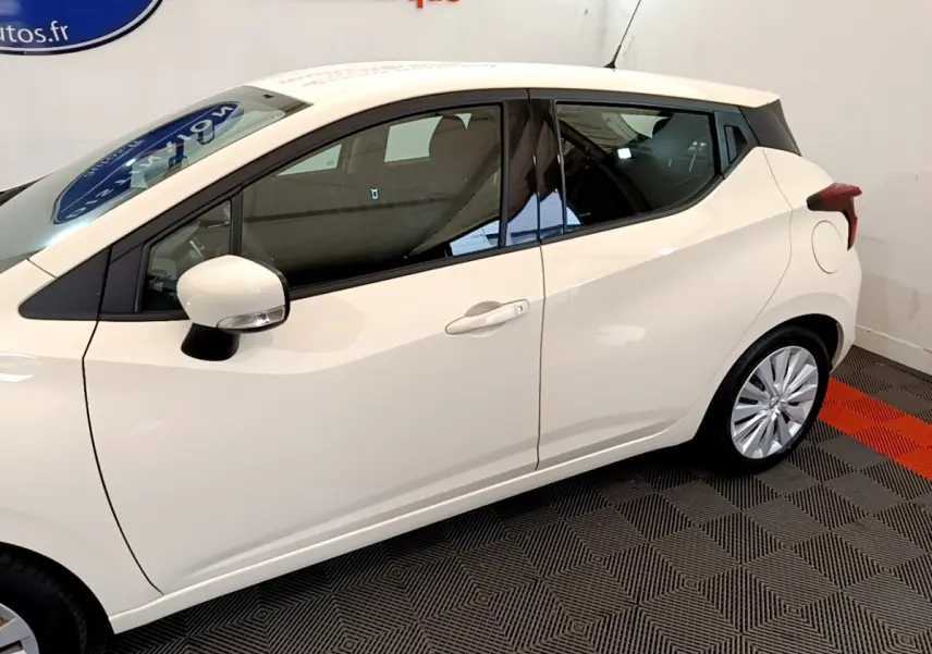 Profil côté gauche d'une Nissan Micra blanche 2022 avec rétroviseur et poignées assortis, sur sol à damier noir et rouge.