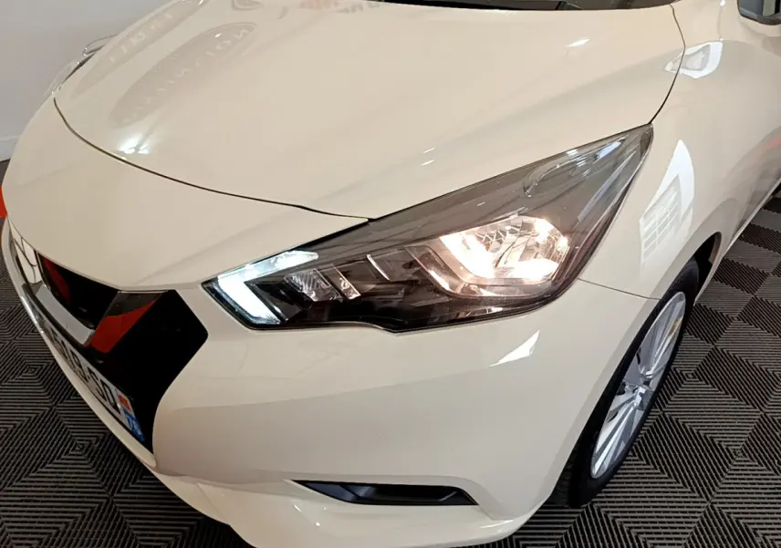 Vue 3/4 avant droit d'une Nissan Micra IG-T 92 Acenta blanche avec phares LED allumés et jantes alliage visibles.